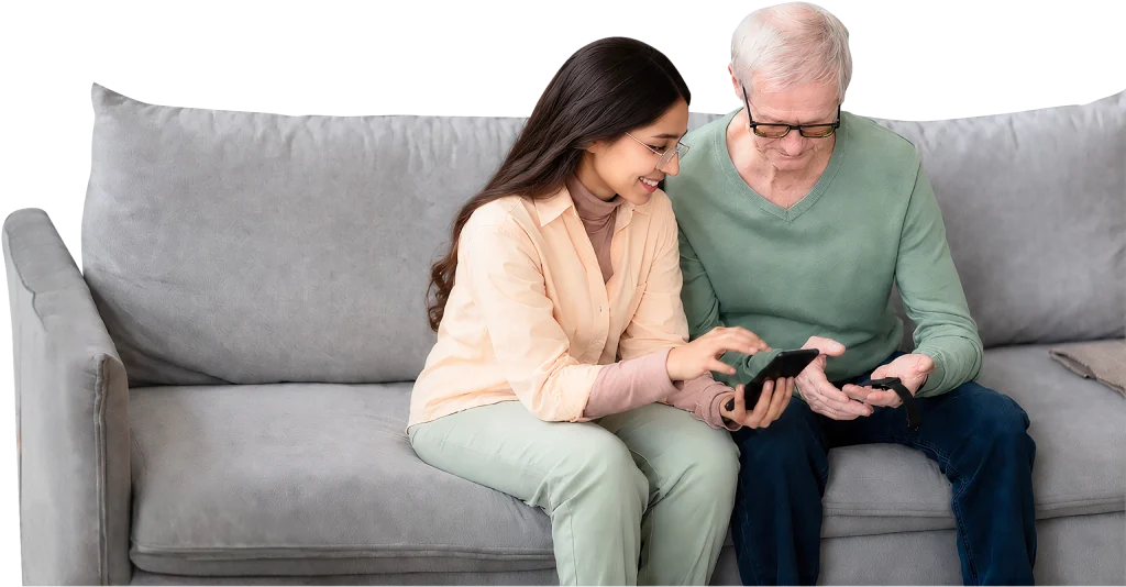 A nurse helping an older patient take a reading with a phone on a sofa